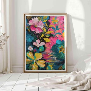 May include: A framed floral art print with bright pink, yellow, and blue flowers set against a pink and dark blue backdrop. The artwork is in a gold frame and displayed on a white floor.