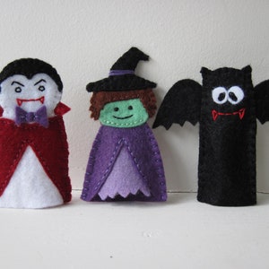 May include: Three felt finger puppets: a vampire with a red cape, a witch in a purple dress and black hat, and a black bat with outstretched wings. The puppets are handmade and suitable for Halloween.