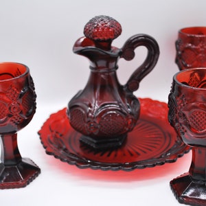 Può includere: Un set di bicchieri in vetro rosso rubino con una caraffa con coperchio, un piatto da portata e tre calici. Il set presenta un motivo in rilievo dettagliato ed è adatto per servire bevande.