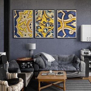 Könnte beinhalten: Drei gerahmte Kunstdrucke mit komplizierten gelben und blauen Mustern hängen über einem grauen Sofa. Die Drucke zeigen sich wiederholende geometrische Designs. Der Raum hat eine moderne Ästhetik mit einem grauen Farbschema und Holzböden.