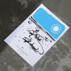 May include: A white print featuring a black and white illustration of a scene with figures and the text "conil de la frontera CADIZ". A blue rectangle with a sun graphic is in the upper right corner.