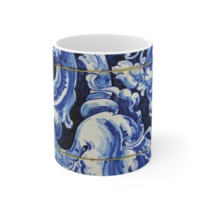 Puede incluir: Taza de cerámica blanca con un diseño floral azul y blanco. El diseño presenta patrones ornamentados y arremolinados en tonos de azul sobre un fondo azul oscuro. Una fina línea dorada rodea la parte superior e inferior de la taza.
