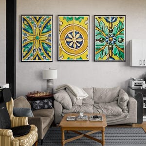 Puede incluir: Tres obras de arte decorativas enmarcadas con coloridos diseños de azulejos florales. La obra de arte presenta tonos amarillos, verdes y azules, añadiendo un toque vibrante a la habitación. Los marcos son negros y el arte se exhibe sobre un sofá.