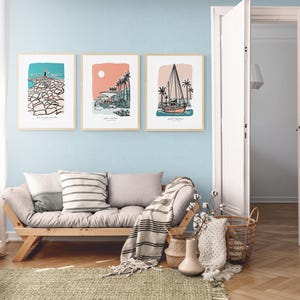 May include: Three framed illustrations of beach scenes with a light blue background. The illustrations are in black and white with pops of color. The illustrations depict a beach with a lighthouse, a beach with palm trees, and a beach with a sailboat.