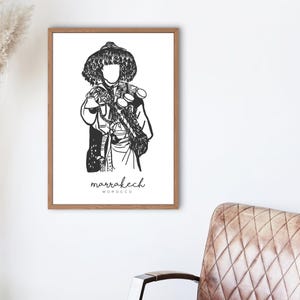 May include: Black and white line art illustration of a person wearing traditional Moroccan clothing. The illustration is framed and includes the text "marrakech MOROCCO".