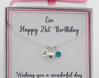 Op de afbeelding: Een witte cadeaudoos met een roze lint en een zilveren ketting erin. De ketting heeft een hartbedel, een bedel met het nummer 21 en een turquoise edelsteenbedel. De doos heeft een kaartje erin met de tekst "Eve Happy 21st Birthday Wishing you a wonderful day Love, Mum and Dad xx"