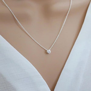 Op de afbeelding: Een delicate zilveren ketting met een klein, rond, helder edelsteen hanger.