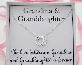 May include: A white gift box with a silver necklace inside. The necklace features two intertwined circles. The box has the text "Grandma & Granddaughter" and "The love between a Grandma and Granddaughter is forever" printed on it.