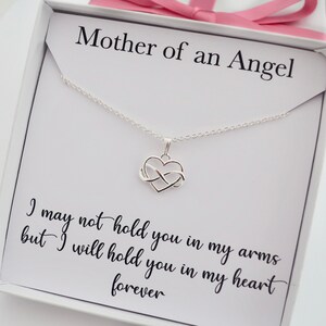 May include: A white box with a silver necklace featuring an infinity heart charm. The box has the text "Mother of an Angel" and the quote "I may not hold you in my arms but I will hold you in my heart forever".