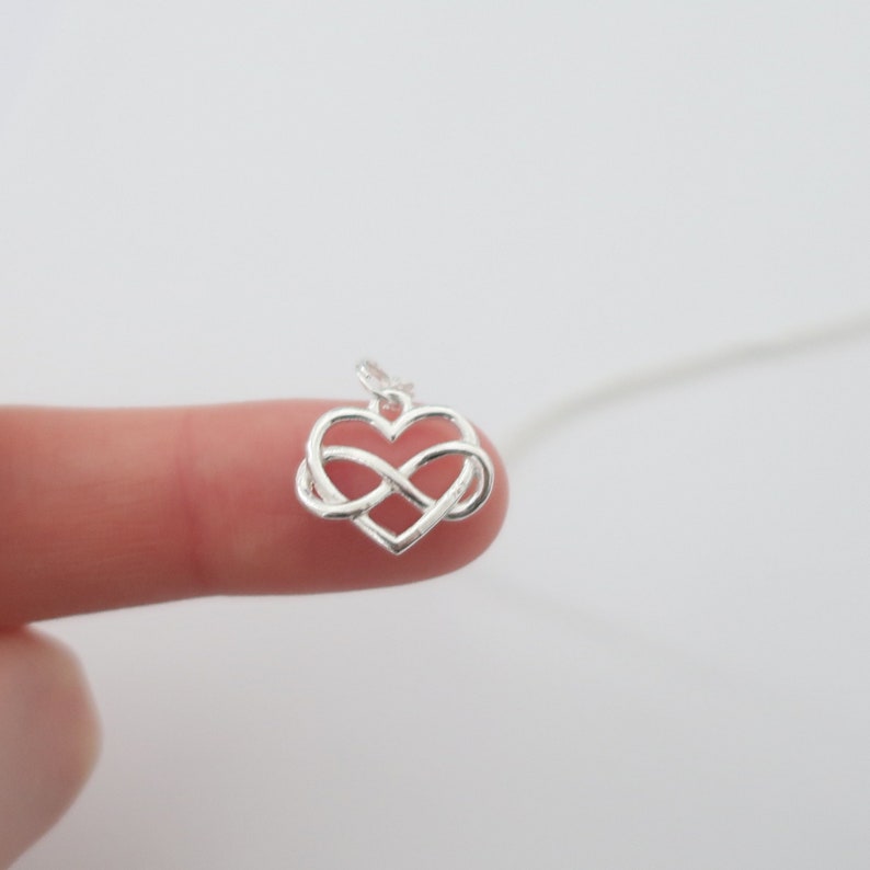 May include: A silver infinity symbol necklace with a heart-shaped design. The pendant is small and delicate, perfect for layering with other necklaces.