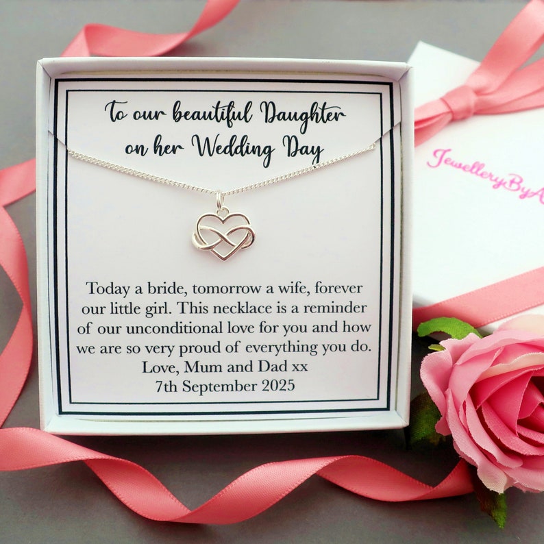 May include: A white gift box with a silver necklace inside. The necklace features an infinity symbol with a heart in the center. The box has a message that reads "To our beautiful Daughter on her Wedding Day. Today a bride, tomorrow a wife, forever our little girl. This necklace is a reminder of our unconditional love for you and how we are so very proud of everything you do. Love, Mum and Dad xx 7th September 2025."