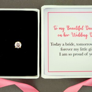 May include: A white gift box with a pink ribbon. The box contains a pair of small, round, clear earrings with gold settings. The box also contains a card with the message "To my Beautiful Daughter on her Wedding Day. Today a bride, tomorrow a wife, forever my little girl. I am so proud of you!"
