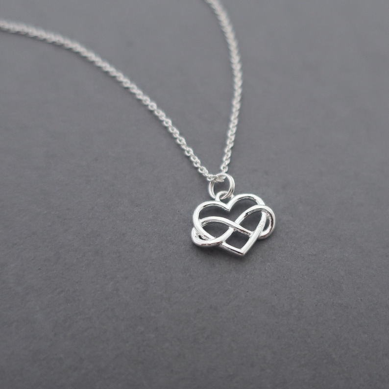 May include: A silver necklace with an infinity symbol pendant in the shape of a heart.