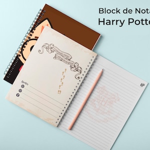 Puede incluir: Dos cuadernos de espiral y un lápiz rosa claro. Un cuaderno tiene una portada marrón con un gráfico, mientras que el otro está abierto en una página con el texto I solemnly swear I am up to no good, huellas y líneas para escribir.