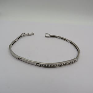May include: A silver bracelet with rectangular links. One section has a row of small, clear stones. The bracelet is unclasped, showing the clasp mechanism. The bracelet is made of silver.