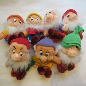 May include: Seven plush toys of the seven dwarfs from the Disney movie Snow White and the Seven Dwarfs. The dwarfs are all wearing different colored clothing and hats.