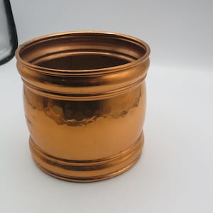 May include: A hammered copper planter with a rounded shape and a slightly flared rim. The planter has a smooth, polished finish and is a warm copper colour.