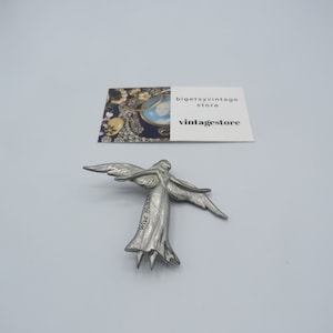 May include: Silver angel brooch with outstretched wings. The angel is wearing a flowing gown and has a delicate face. The brooch is inscribed with the words "Wise Woman".