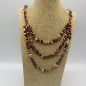 May include: A multi-strand necklace made of brown, red, and white stone chips. The necklace is layered and hangs to the chest.
