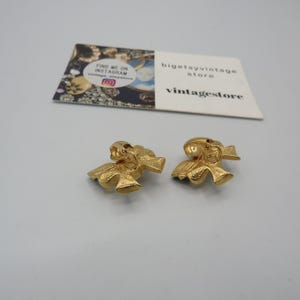 May include: A pair of gold-tone bow-shaped clip-on earrings. The earrings are made of metal and have a textured surface.