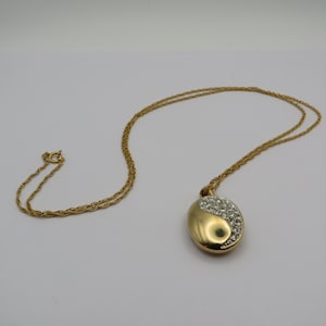 May include: A gold-coloured necklace featuring a pendant in a yin-yang design. One half of the pendant is encrusted with clear crystals, the other is smooth gold. The chain is a fine rope style, and the clasp is visible.