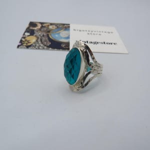 May include: A silver ring featuring a large, oval-shaped turquoise gemstone. The ring has a textured band and a delicate, openwork design.