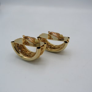 Peut inclure: Une paire de boucles d'oreilles clips dor&eacute;es avec un design textur&eacute; et tiss&eacute;. Les boucles d'oreilles ont la forme d'un demi-cercle.