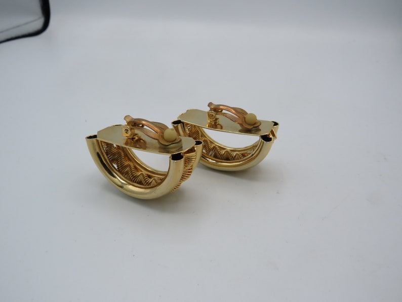 Peut inclure: Une paire de boucles d'oreilles clips dor&eacute;es avec un design textur&eacute; et tiss&eacute;. Les boucles d'oreilles ont la forme d'un demi-cercle.