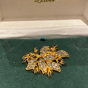 May include: A gold-toned brooch with black enamel accents and clear rhinestones in a floral design. The brooch is in a green velvet box with the inscription "Leslie Davis".