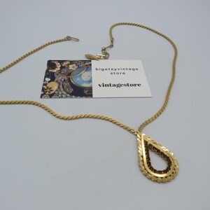 Puede incluir: Collar dorado con un colgante en forma de lágrima. El colgante está relleno de pequeñas piedras de color rojo oscuro y enmarcado por un borde dorado texturizado. La cadena del collar tiene un diseño de cuerda trenzada. También hay una tarjeta de visita con el texto "bigetsyvintage store vintagestore".