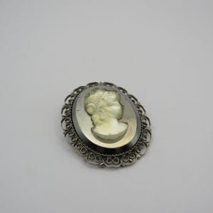 Può includere: Spilla cammeo ovale raffigurante il profilo di una donna con i capelli ricci. Il cammeo è incastonato in una cornice in filigrana argentata. La spilla è un pezzo vintage, probabilmente dell'epoca vittoriana, ed è un gioiello classico.