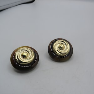 Könnte beinhalten: Ein Paar runde Ohrringe in Braun und Gold mit einem Spiralmuster. Die Ohrringe sind rund und haben eine goldene Mitte mit einem Spiralmuster.