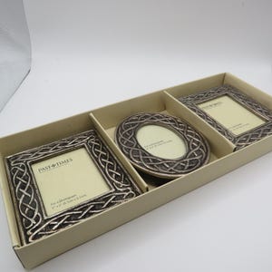 May include: A set of three Past Times picture frames in a beige cardboard box. The frames feature a silver-toned metallic finish with an intricate Celtic knotwork pattern. The set includes one square frame, one oval frame, and one rectangular frame.