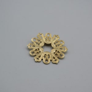 Può includere: Un pezzo decorativo in metallo dorato con un design circolare traforato. Il pezzo presenta un motivo delicato e intricato con un motivo floreale.