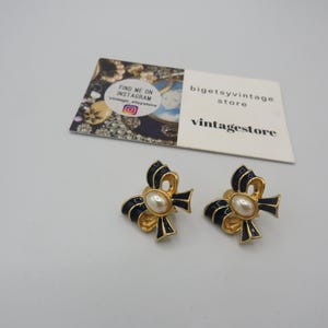 May include: A pair of gold tone earrings with a blue enamel bow and a pearl centre. The earrings are clip-on style.