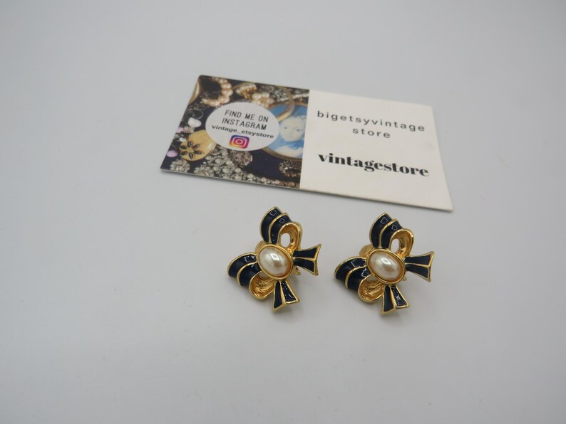 May include: A pair of gold tone earrings with a blue enamel bow and a pearl centre. The earrings are clip-on style.