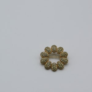 Puede incluir: Un broche dorado en forma de flor con brillantes transparentes.