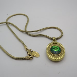 May include: A gold-toned necklace with a pendant featuring a green iridescent stone. The oval pendant is set in a textured, gold-colored frame. The chain is a thin, snake-style design.