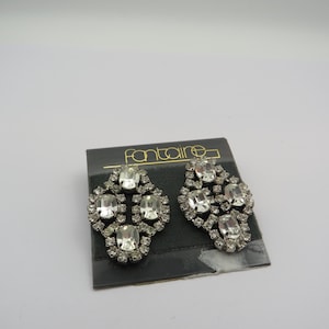 May include: A pair of vintage Fontaine rhinestone earrings. Each earring features a cluster of clear, oval and round rhinestones set in a silver-tone metal. The earrings are displayed on a black card with the Fontaine logo.