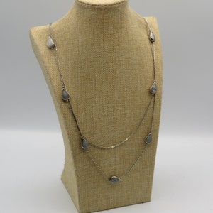 Puede incluir: Un collar de cadena de plata con múltiples hebras y colgantes en forma de lágrima. Los colgantes son de color gris claro.