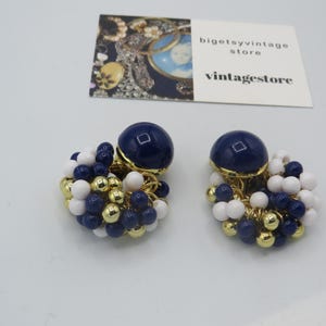Könnte beinhalten: Ein Paar blaue und weiße Perlen-Ohrringe mit goldenen Akzenten. Die Ohrringe haben oben eine große blaue runde Perle und darunter einen Cluster aus kleineren blauen und weißen Perlen.