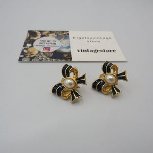 May include: A pair of gold tone earrings with a black enamel bow and a faux pearl centre.