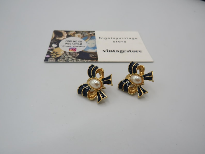 May include: A pair of gold tone earrings with a black enamel bow and a faux pearl centre.