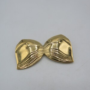 Può includere: Un fermaglio in metallo dorato a forma di fiocco. Il fiocco ha un design testurizzato e ondulato.