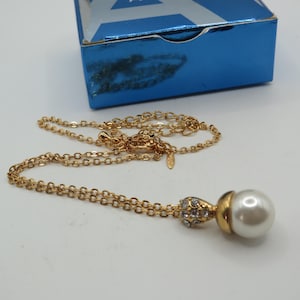 May include: A gold-tone chain necklace featuring a pendant with a single white faux pearl attached to a gold-tone cap encrusted with small clear crystals. The necklace includes a lobster claw clasp and an adjustable extender chain with a small tag.
