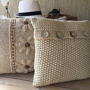 May include: Two knitted throw pillows, one with a crocheted floral design and the other with a simple knit texture and decorative buttons.
