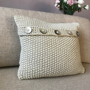May include: A cream-colored knitted pillow with a row of five decorative buttons.