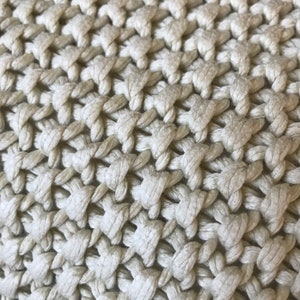 May include: Close-up of a beige knitted fabric with a textured, woven pattern.