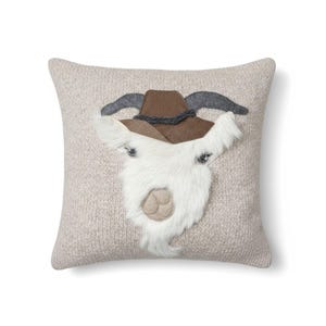 May include: A square decorative pillow with a light beige knitted texture. The pillow features a goat face design with a brown cowboy hat, gray horns, and a white furry beard. The goat's eyes are small and dark.
