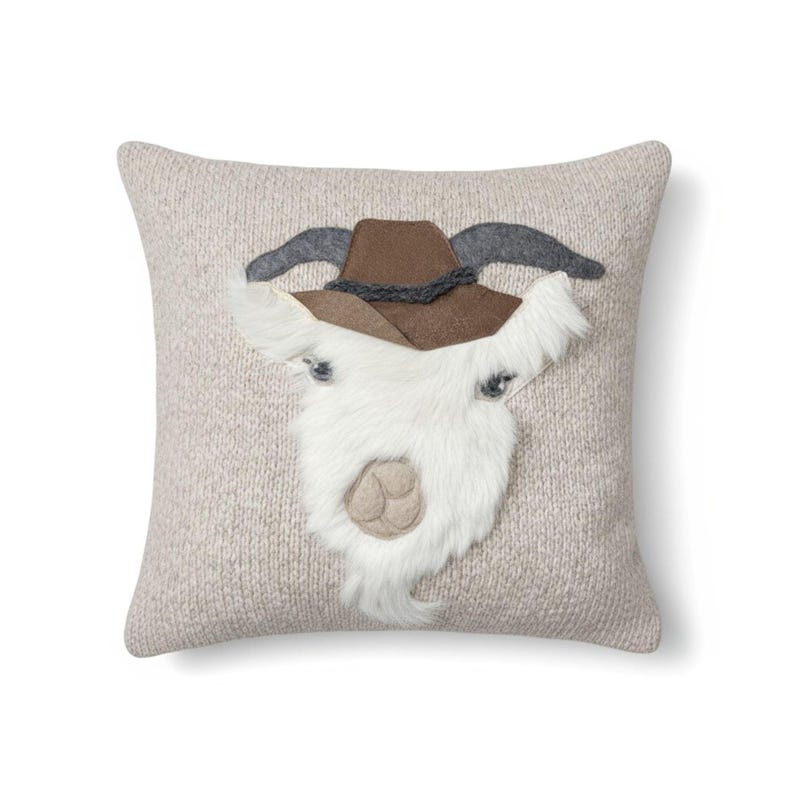 May include: A square decorative pillow with a light beige knitted texture. The pillow features a goat face design with a brown cowboy hat, gray horns, and a white furry beard. The goat's eyes are small and dark.